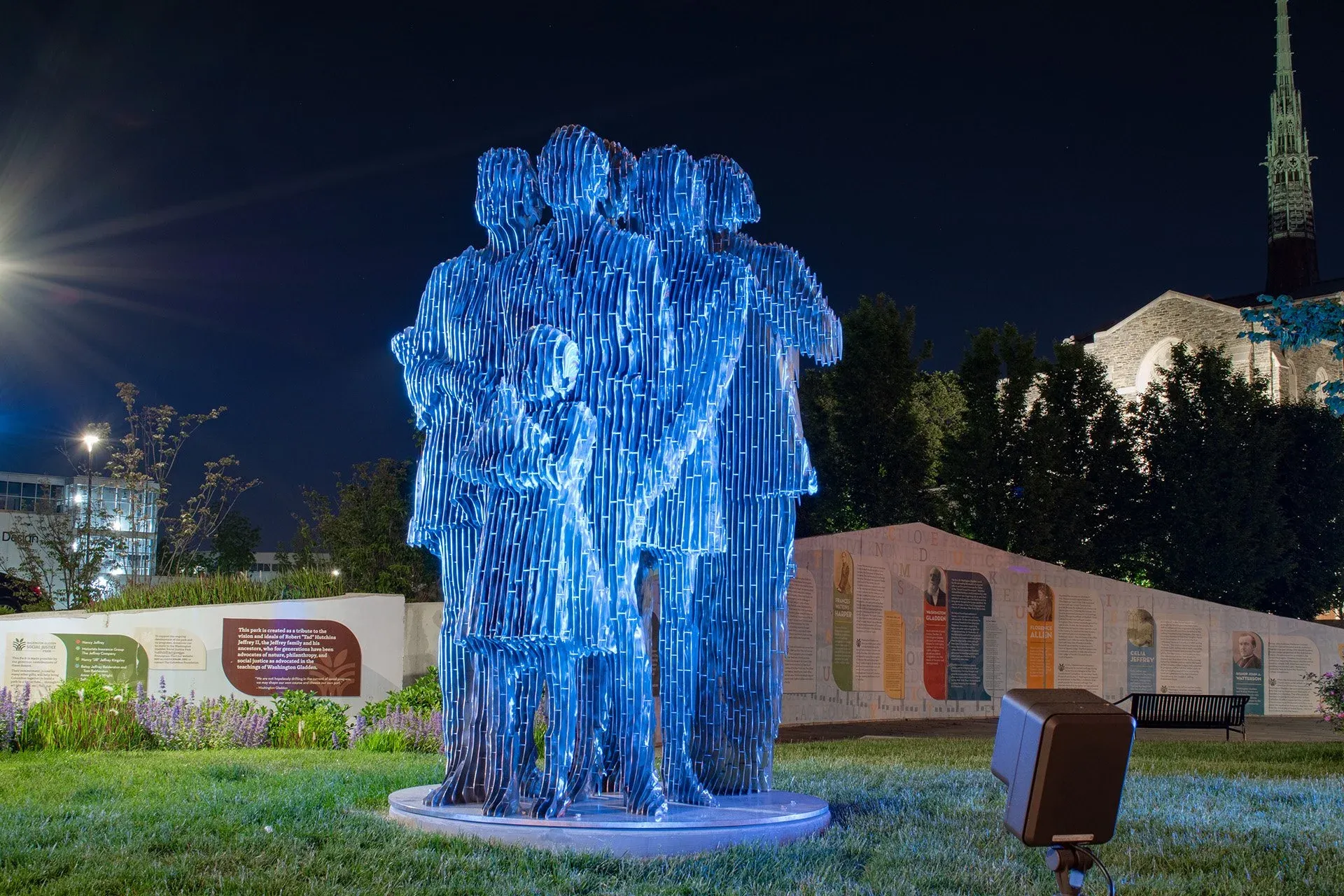 A sculpture of figures standing together, lit in blue at night.